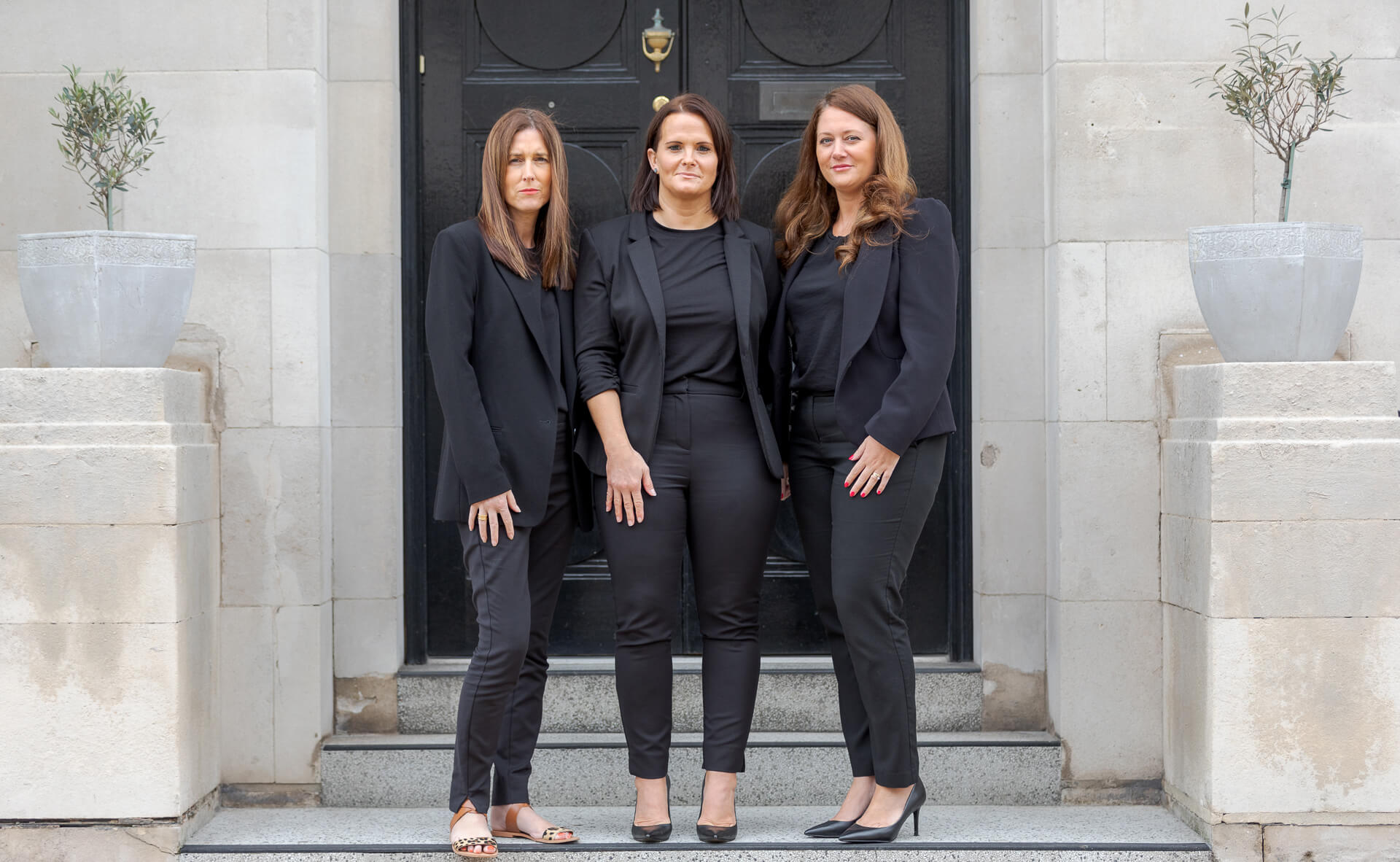 3 women standing aside each other in front of a door