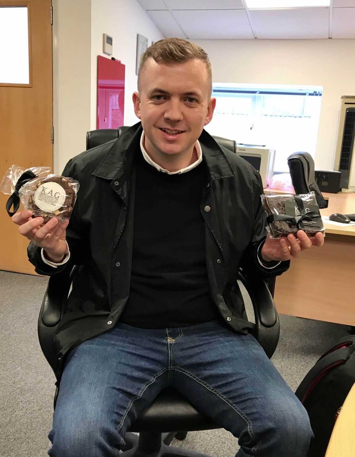 a man wearing black shirt and black jacket and holding chocolates in both hands