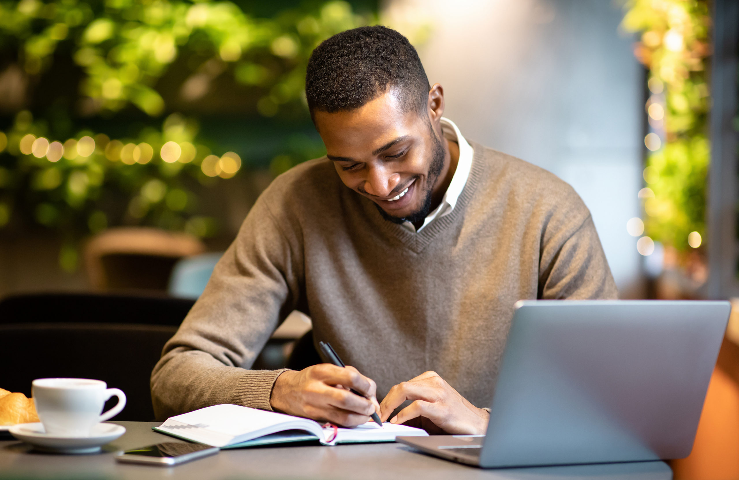 Black man writing in notebook sitting at cafe man headshot